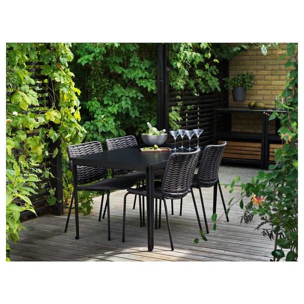 Outdoor dining set with dark grey wicker chairs and rectangular table, surrounded by lush greenery.