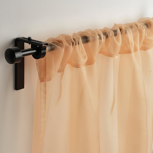 Light-filtering curtains in pale orange hang from matte black rod, tailored with pocket design for easy instal.
