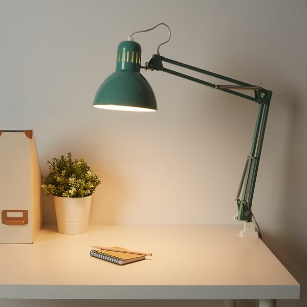 Adjustable green desk lamp illuminating notebook on a tidy workspace.
