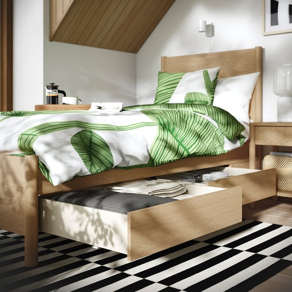 Cosy bedroom with a wooden TONSTAD bed, featuring green leaf bedding and soft-closing under-bed storage drawers.