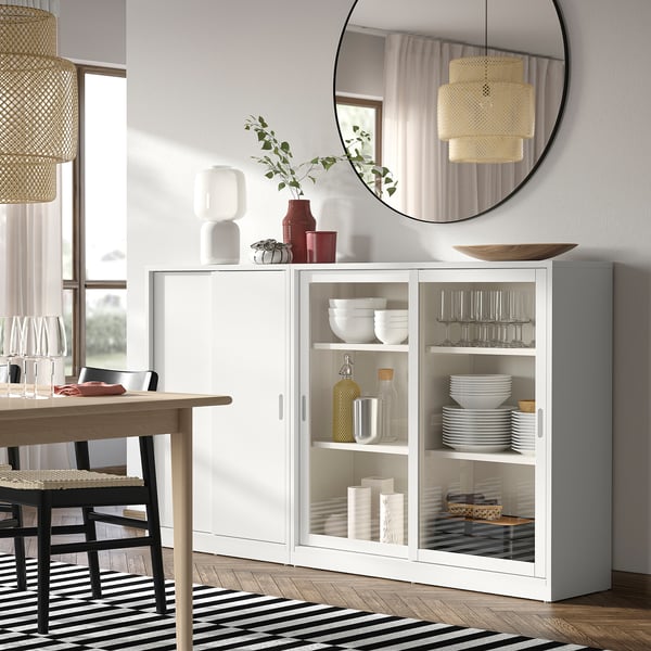 TONSTAD off-white cabinet with sliding doors displays dishes. Round mirror, woven lamp, black & white rug on wood floor.