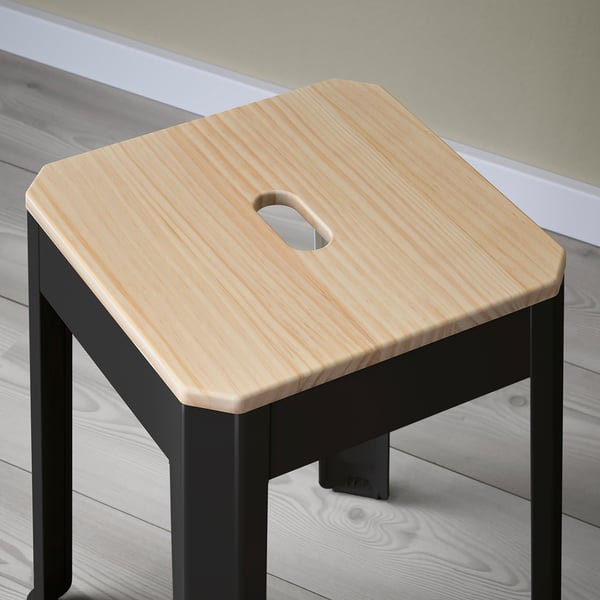 Small, sturdy stool with light wooden seat and black metal legs, showcasing fine craftsmanship and a practical handle cutout.