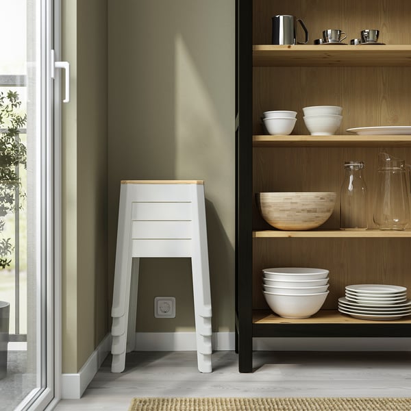 Small, white stackable stool near wooden shelves with dishes. Stool has cutout handle for easy carrying.