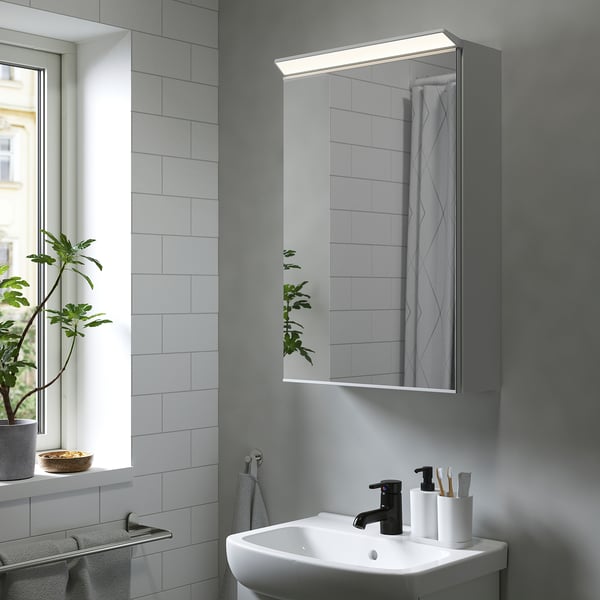 TREASJÖN mirror cabinet in bathroom offers storage and lighting above sink, with plant on window sill.