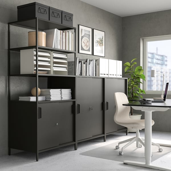 Black office cabinet, chair, desk with laptop, window, grey walls, artwork.