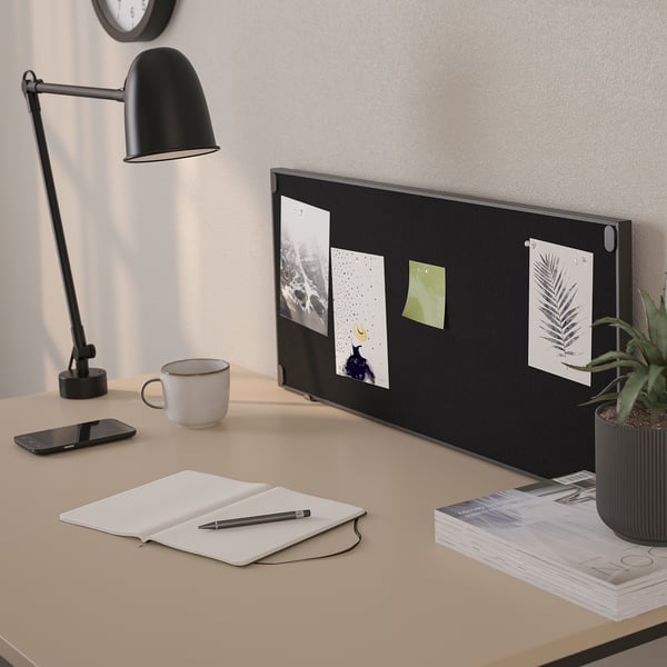 Desk with black lamp, open notebook, pen, phone, mug, plant, and double-sided board with photos and notes.