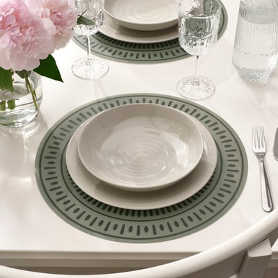 Table set with green patterned placemats, white dishes, glasses, silverware, and pink flowers.