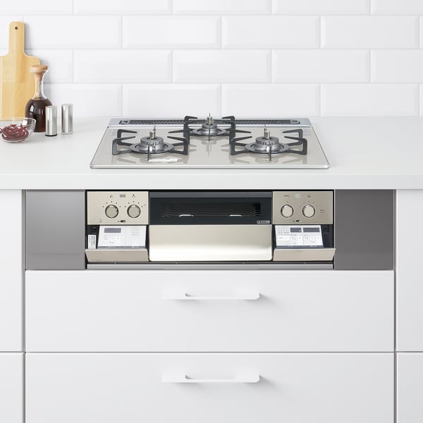 Small, metallic, modern kitchen stove with four burners, control panels, and digital displays matching clean white countertop and backsplash.