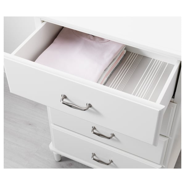 White chest of drawers with silver handles, showing an open drawer containing neatly folded clothes and a divider.