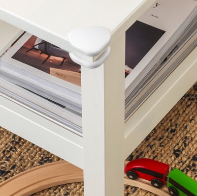 White corner bumpers on table edges for child safety. Magazines and toy cars on table.