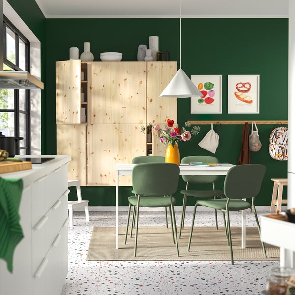 Modern kitchen with green walls, wooden cabinets, white dining table VIHALS, four green chairs, hanging lamps, vibrant art, and terrazzo-style floor.