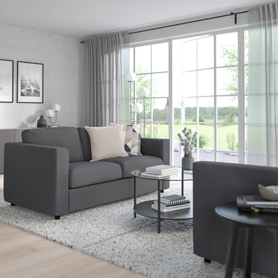 Minimalist living room: grey VIMLE sofa near large window, modern decor, wooden floor, light rug.