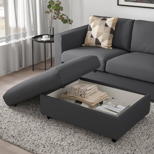 Modern grey sofa with cushions & footstool. Coffee table with blankets & magazines, side table with cup. Minimalist living room.