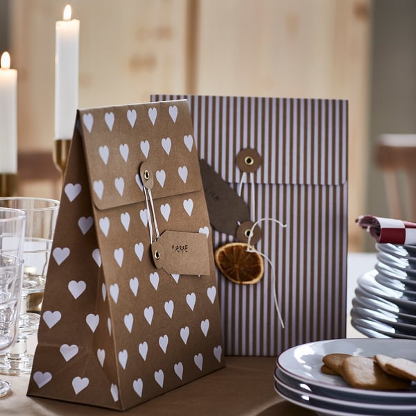 Decorative gift bags with hearts and stripes on a dinner table, accompanied by candles and cookies.