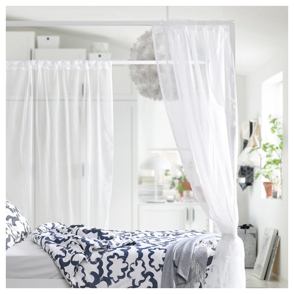 Bright, white canopy bed with blue patterned sheet, surrounded by sheer white curtains, offering a cosy, private nook.