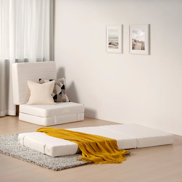 Foldable VITHÄLL guest bed with pillows, on black/white rug, minimalist room, coastal wall art.