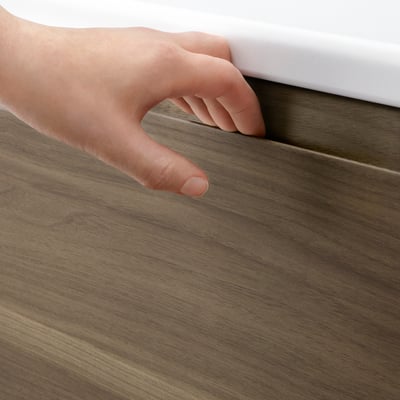 A hand opens a wooden cabinet door with a smooth, dark walnut finish, showcasing its easy-to-use integrated handle.