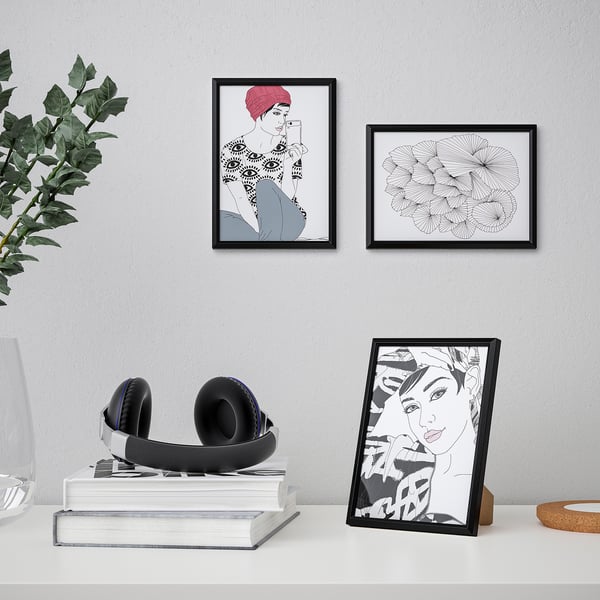 A frame displayed on a table with artwork, standing, and featuring a picture of a stylized person; additional framed artworks hang on the wall.