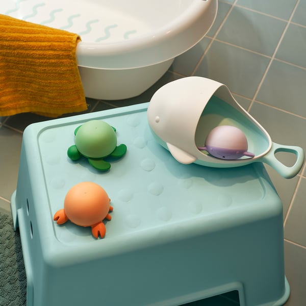 A blue bathroom step stool with a green turtle, orange crab, and whale bath toys on it.
