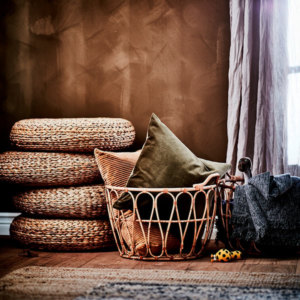Hand-woven ALSEDA stools stacked, olive green pillow, wooden floor, natural colours, cosy decor.