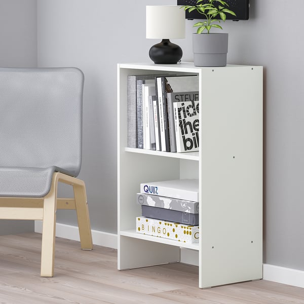 White bookshelf against wall with lamp, plant, books, and games.
