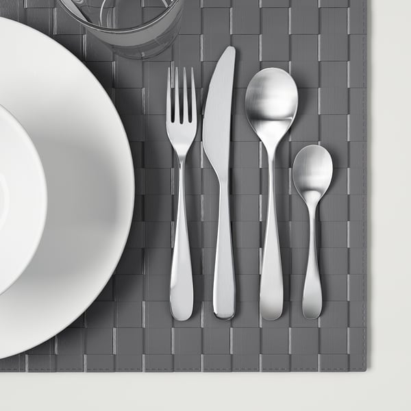 Silverware set on grey placemat: fork, knife, large and small spoons.