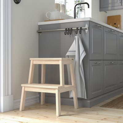 Minimalist wooden step stool in natural wood beside grey kitchen cabinets, blending size with surroundings.