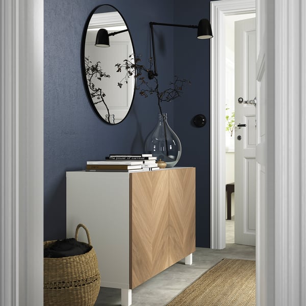 Modern entryway with BESTÅ sideboard, mirror, lamps, and decor against dark blue wall.