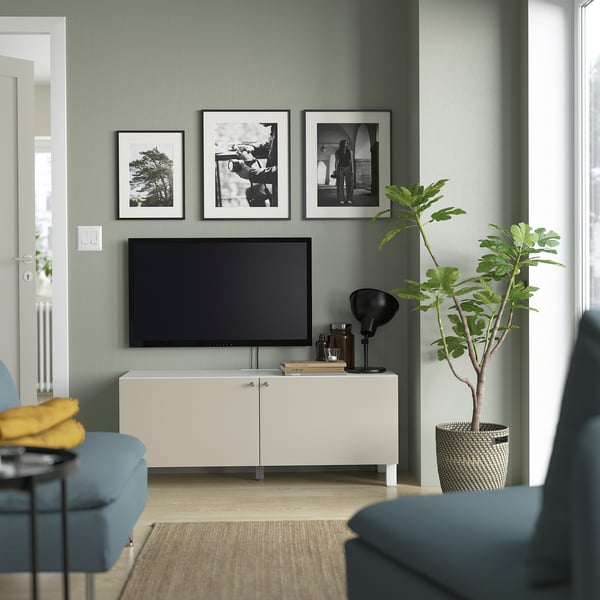 Modern living room with BESTÅ tv bench, blue sofa, flat screen tv, black lamp, and green plant. Light green wall, cosy seating.