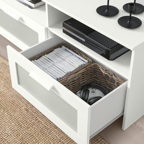 Open white tv stand drawer reveals organised gaming controllers and game cases in divided baskets. Console placed on stand.