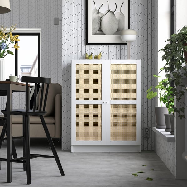 Modern living space with white and grey decor, featuring a BILLY bookcase with bamboo doors, a grey sofa, black chairs, and a stylish plant.