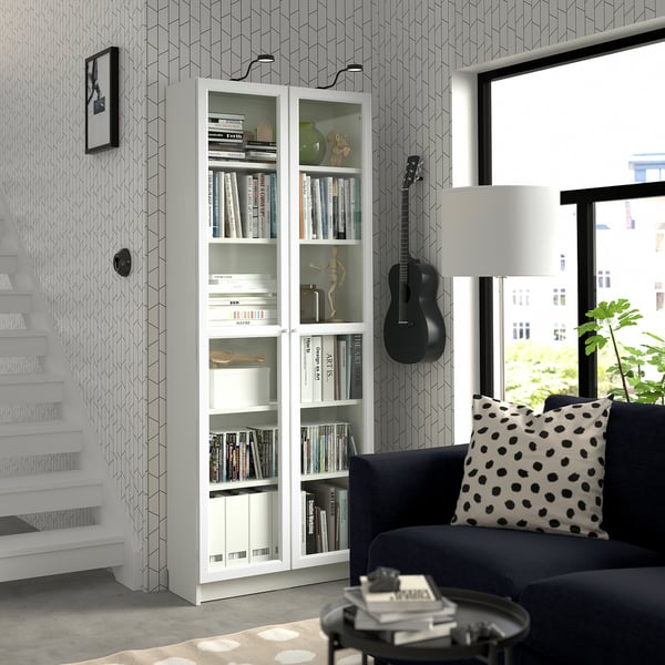 Modern living room with BILLY bookcase, blue sofa, guitar, and geometric wallpaper.