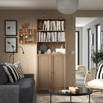 Modern living room with grey sofa, wooden BILLY bookcase filled with books, and decorative items.