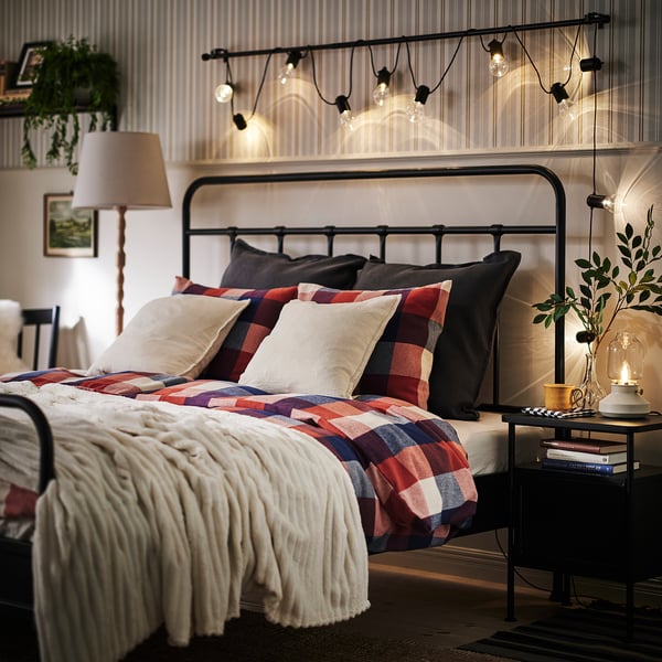 Cosy bedroom with chequered bedding, white blanket, and ambient string lights.