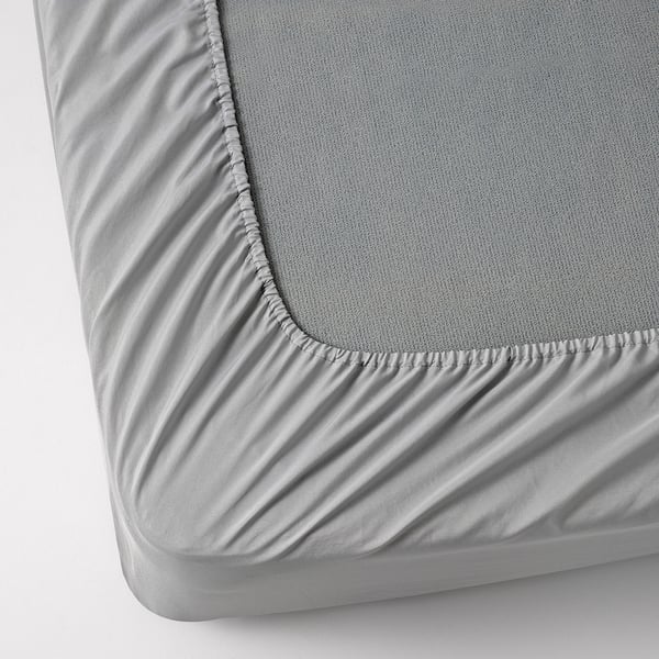 Close-up of a fitted bed sheet with elastic edges. Soft, breathable fabric over a thick mattress. Shows detailed stitching and material texture.