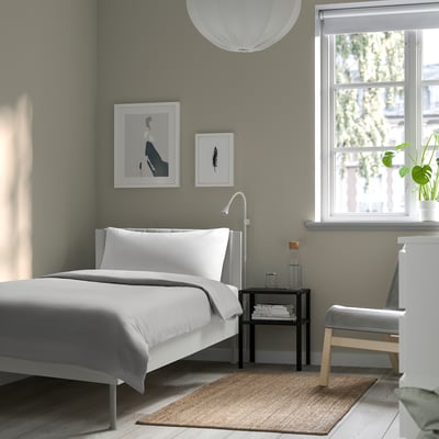 Modern minimalist bedroom with white BRUKSVARA bed, grey walls, large window, and pendant light.