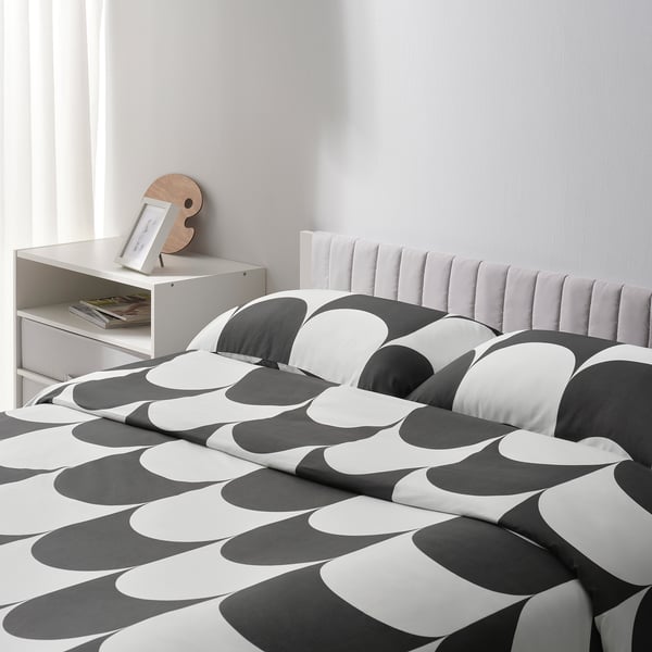 Bed with striped quilt, white headboard, storage shelf with books, and circular wooden decoration.