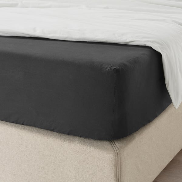 Bed with black fitted sheet on white mattress, showing elastic edging, suitable for 26 cm thick mattresses.