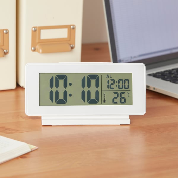 Digital alarm clock on desk, displaying time 10:10, alarm 12:00, and temperature 26°c. Has led backlight and snooze function.