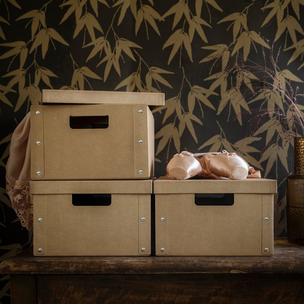 Three beige GÄRDESGÅRD storage boxes, stacked. Middle box holds ballet shoes, on wooden shelf. Dark bamboo pattern wall.