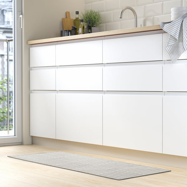 Modern kitchen with GATUSEKTION mat. Grey & white stripes, fits under sink. Sits on light wooden floor.