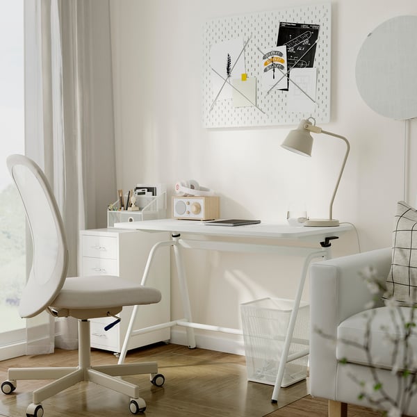 Compact home office setup: GLADHÖJDEN standing desk, swivel chair, lamp, pegboard, armchair.