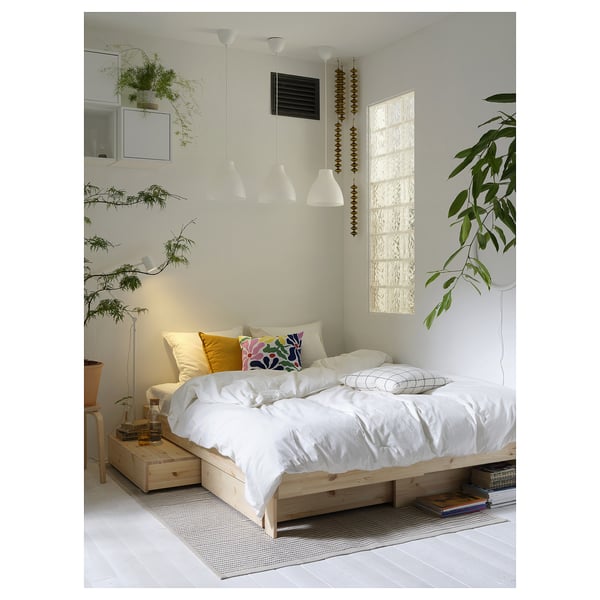 Bedroom with white bedding, colourful pillows, hanging plants, and white lamps above.