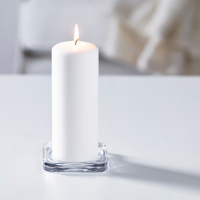 A lit white candle in a clear, wavy glass holder, creating ambiance.