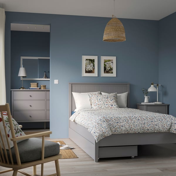 Blue bedroom with grey gullberg bed, wooden floor, wicker lamp, art, rocking chair, and dresser. Cosy and harmonious.