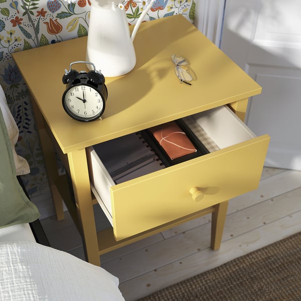 Bright yellow GULLABERG bedside table with open drawer, clock, glasses, and white vase.