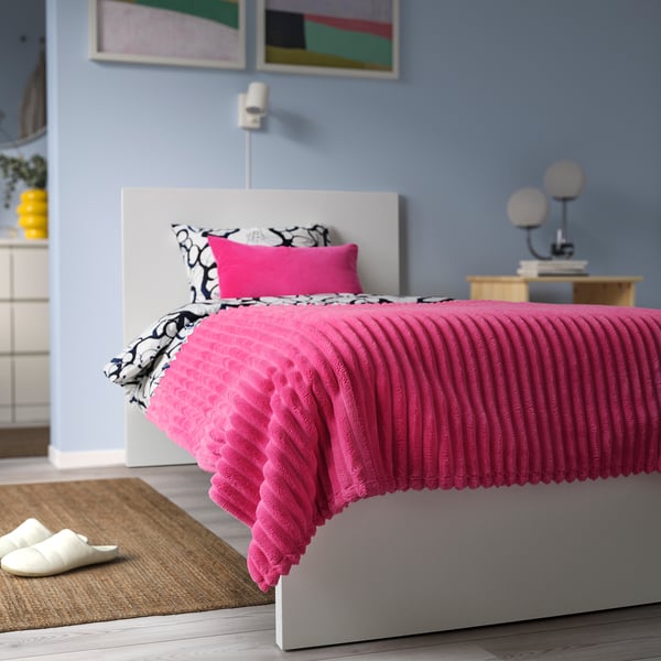 Bright pink GULLSTRÅLE fleece bedspread covers a double bed, appearing soft and fluffy, larger than surrounding nightstands.
