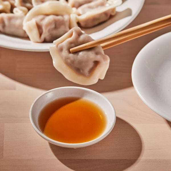 Small dish holding orange sauce, accompanied by dumplings and chopsticks on a wooden table.