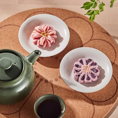Two flower-shaped pastries on plates beside a teapot and cup on a circular tray.