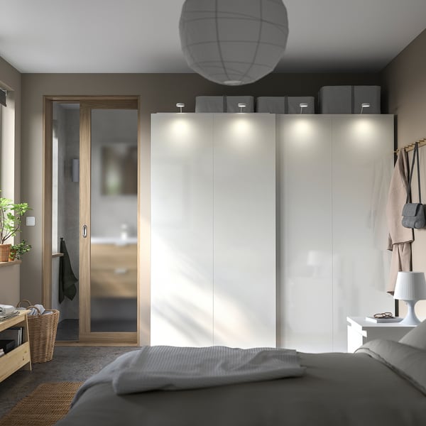 Modern bedroom with glossy white HASVIK sliding wardrobe, grey bedding, wooden accents, and soft lighting.